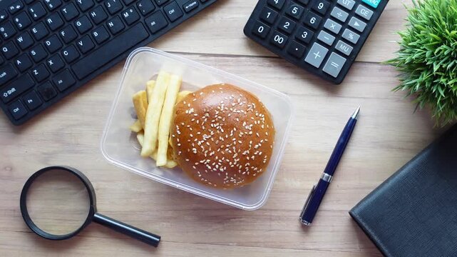 Business lunch on office desk with burger and fries in plastic container on wooden table
