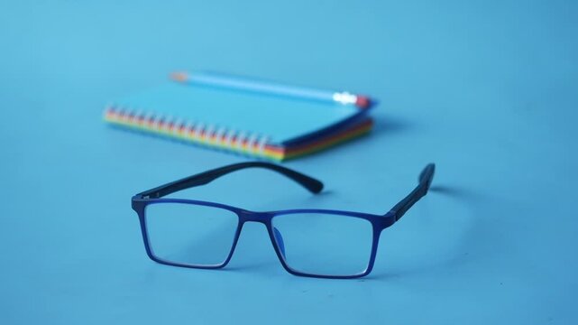 Pair of modern spectacles with blue frames resting on table with colorful notebook in background