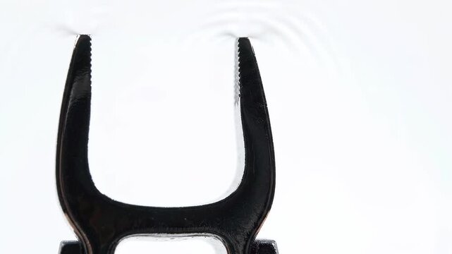 Black pliers tips touching water surface creating spreading ripple waves. Tool and liquid interaction. Slow motion water circles on white background