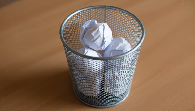 Metallic mesh trash bin filled with discarded white paper balls for office organization and waste disposal.
