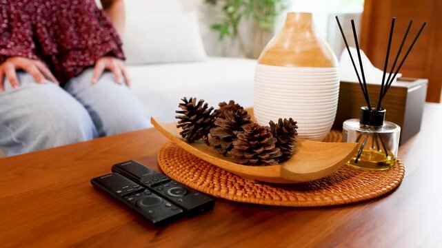 A woman's hand reaching to pick up tv remote control on wooden table in living room at home, modern interior design background, cinematic motion footage.