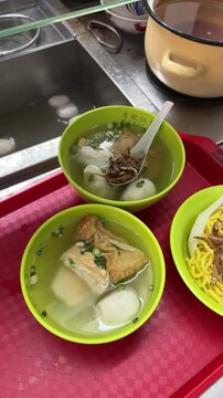 bowls of yong tau foo soup with fish balls, tofu, and stuffed vegetables topped with fried ikan bilis, served in green bowls on a red tray at a hawker stall. traditional Singapore street food