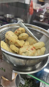 freshly cooked yong tau foo pieces draining in a metal mesh strainer with ladle, showing fish paste stuffed ingredients speckled with herbs and chili. traditional Singapore hawker food preparation