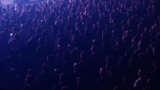 Large audience enjoying live music at an indoor entertainment concert venue. Flashing colorful lights, people dancing and watching the band perform on stage. General admission floor section.