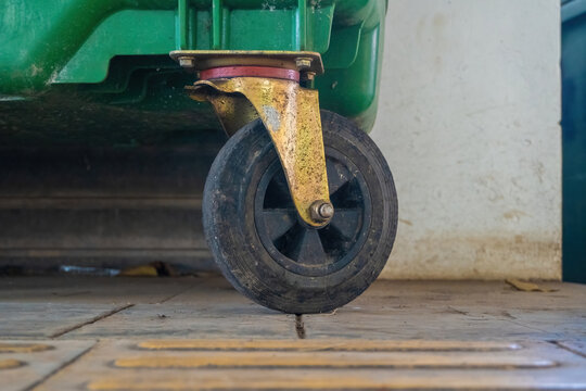 Close up of a heavy duty black rubber swivel caster wheel mounted under a commercial green waste dumpster bin.