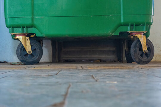Low angle view of heavy duty rubber swivel caster wheels mounted under a large green commercial waste dumpster container standing on a tiled floor.