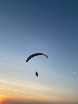 Paramotor pilot flying silhouette against sunset sky gradient