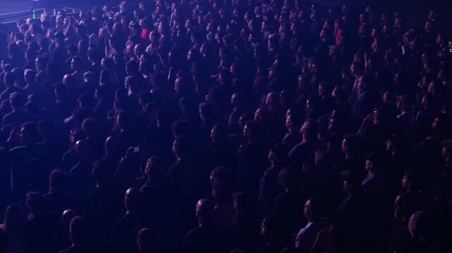 Audience enjoying live music at an indoor entertainment concert venue. Flashing colorful lights, dancing and watching the band perform on stage. General admission floor section.