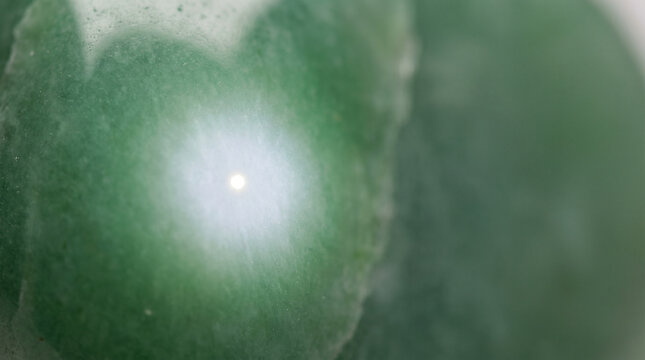 Close-up of a focused bright analysis beam point on a polished green mineral surface, representing synchrotron X-ray measurement, quiet scientific macro photography 