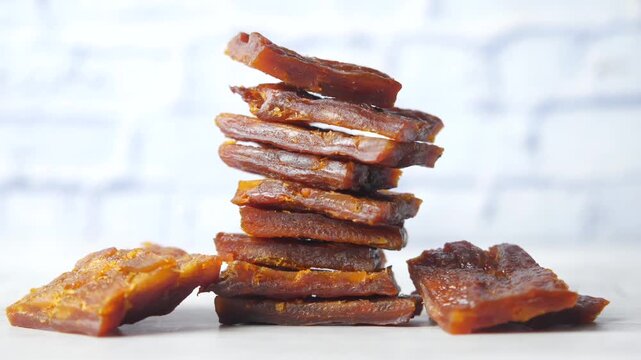 Close up of dried meat slices stacked on white table with brick wall background