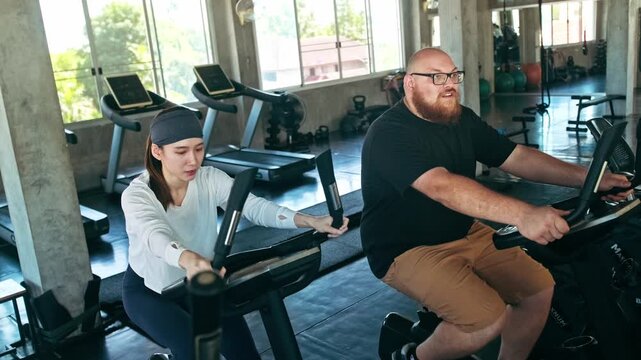 Man and woman exercise side by side on stationary bikes in a modern gym, focusing on cardio training, endurance, motivation and an active healthy lifestyle together.