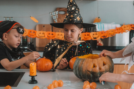 A portrait of a young girl and her younger brother celebrating Halloween and carving pumpkins in the kitchen with their mother's help. They are dressed in witch and pirate costumes. 