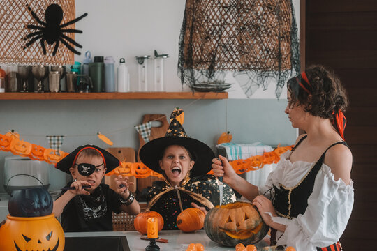 A portrait of a young girl and her younger brother celebrating Halloween and carving pumpkins in the kitchen with their mother's help. They are dressed in witch and pirate costumes. 
