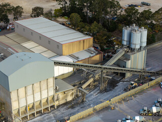 Concrete batching plant with aggregate silos, enclosed conveyors, production buildings and cement mixer trucks forming a complex industrial construction materials facility © Paul Tama