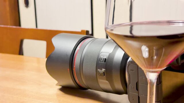 Close-up shot of a wine glass and camera lens on a wooden table, dynamic shot.