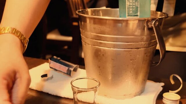 Bartender pouring alcoholic drink into shot glass from bottle chilling in ice bucket.