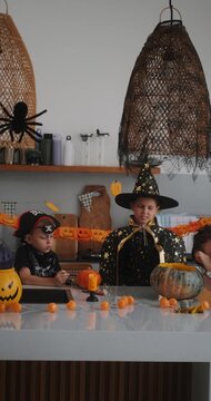 A portrait of a young girl and her younger brother celebrating Halloween and carving pumpkins in the kitchen with their mother's help. They are dressed in witch and pirate costumes. 