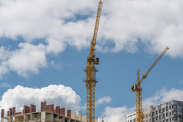Modern construction cranes tower over a vibrant cityscape under a bright blue sky with fluffy clouds © beholdereye