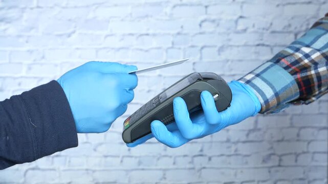 Person wearing blue gloves holding payment terminal and inserting credit card for contactless payment