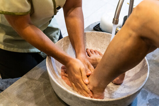 Close-up of masseuse washing customer's feet and legs with water and soap before performing traditional Thai foot and leg massage in salon.
