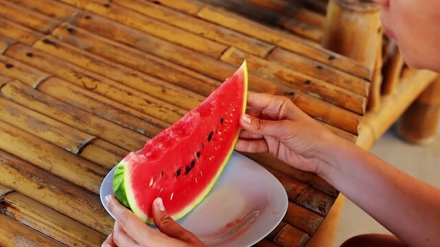 Side view of the woman eating water melon sitting at the wooden table