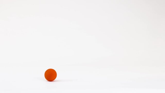 Orange ping pong ball bouncing across white background in slow motion studio footage.