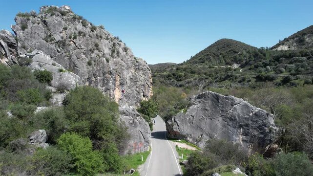 Drone footage revealing a person climbing a sheer rock face next to a winding mountain road. Hasamboulia rock formation Paphos Cyprus