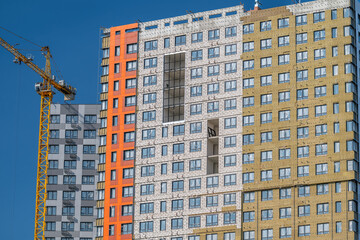 Urban construction scene showcasing modern architecture with a vibrant orange accent in a high-rise building against a clear blue sky © beholdereye
