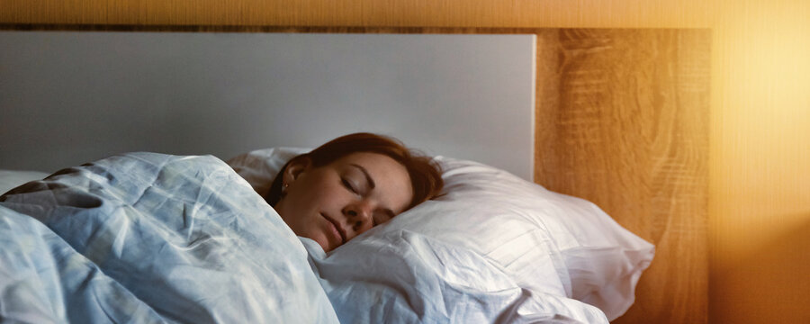 A woman peacefully sleeps in a cozy bed in a hotel room, snuggled under a white duvet. She rests soundly, enjoying a morning nap after a long day of travel.