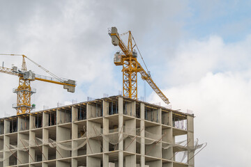 Construction cranes tower over a new building project against a blue sky with fluffy clouds © beholdereye