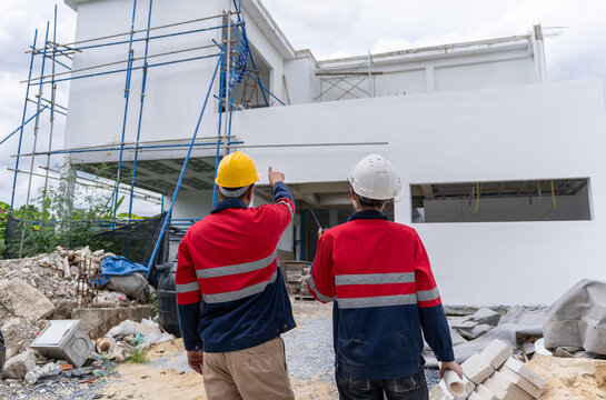 Engineering team wearing hardhats and red safety jackets discussing and inspecting at a construction site.