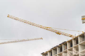 Construction cranes tower over a developing building site under a cloudy sky © beholdereye