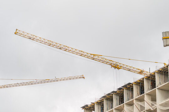 Construction cranes tower over a developing building site under a cloudy sky