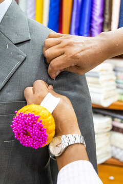 Close-up of professional tailor adjusting and refining new suit with needles to have perfect fit for client in shop before sewing and delivering perfectively fit clothing for client