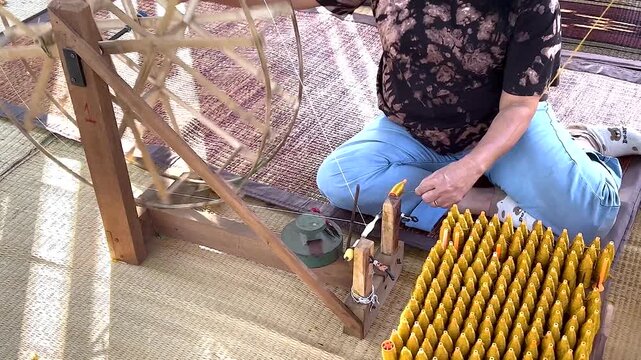 Asian woman spinning silk thread on traditional wooden wheel tool in Thailand.