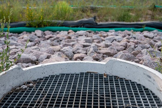 a concrete storm drain inlet surrounded by small grey and pinkish rocks and silt socks in the distance. civil engineering background