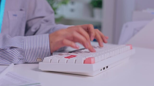 Office worker typing on computer keyboard at desk with focused hand movement, paperwork, monitor, soft purple lighting, technology, and clean professional workplace scene