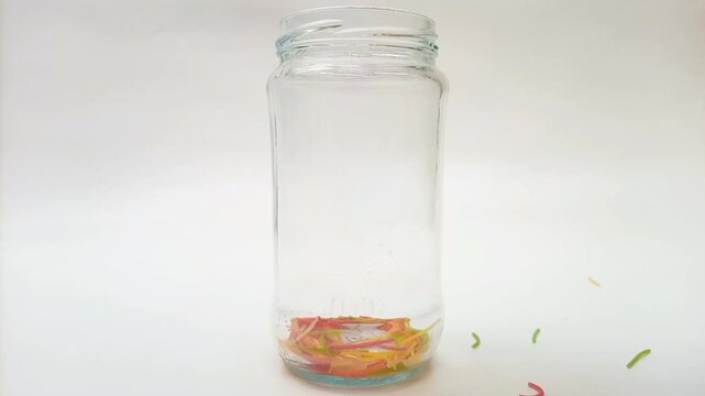 Colorful Vermicelli pasta falling in a glass Jar isolated on white background. Dry uncooked Seviyan. Multicolored Filini pasta