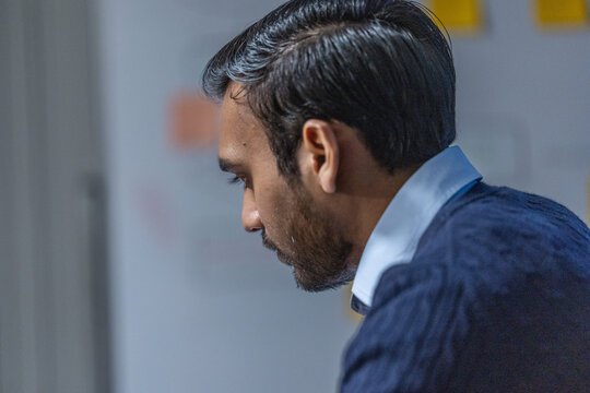 A bearded developer in a navy knit sweater keeps his eyes lowered as he reads a long stack trace against a soft grey studio backdrop on a long night of debugging and deployment.