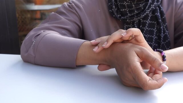 Woman checking her pulse in a close-up shot, seated at table, showing health awareness and body monitoring