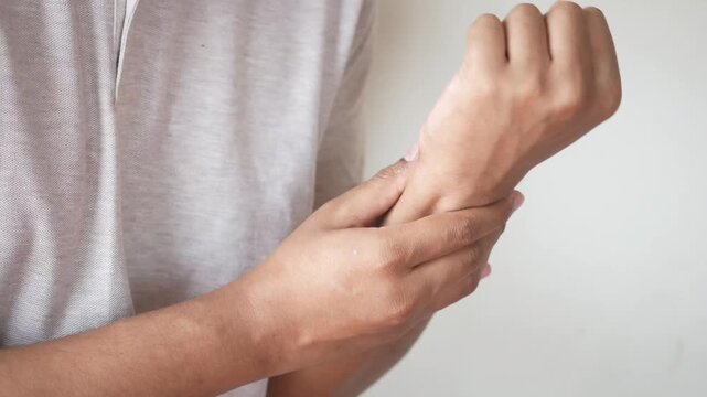 Close up video of person in grey shirt rubbing and massaging painful wrist on a plain background, showing discomfort and need for relief due to injury