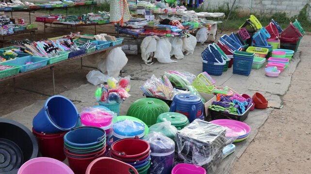 Outdoor market stall display of colourful plastic buckets and household items.