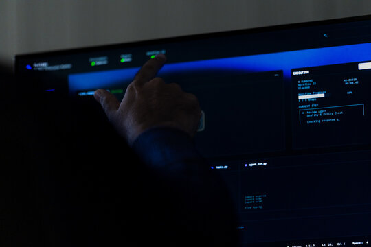A detailed shot of an outstretched finger selecting a panel on screen frames the exact moment a control is selected on the interface in a quiet corporate office during a busy evening shift