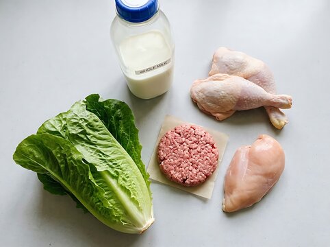 Fresh ingredients including chicken, lettuce, and milk for healthy meal preparation on clean surface