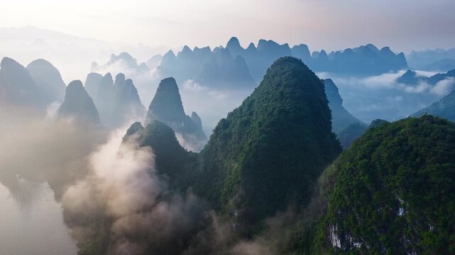 High angle view of limestone karst peaks rising above morning fog near a river in Guilin, Guangxi, China, illuminated by soft sunlight.