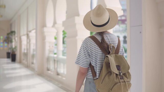 Female tourist in hat with backpack is walking along galleria