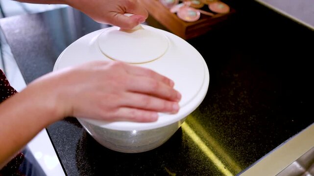 Woman hands spinning salad in manual white plastic centrifuge on kitchen counter.