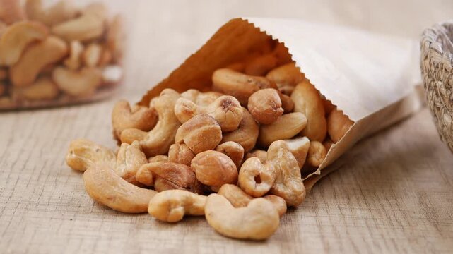 A paper bag filled with cashews tips over, and the nuts scatter across the table