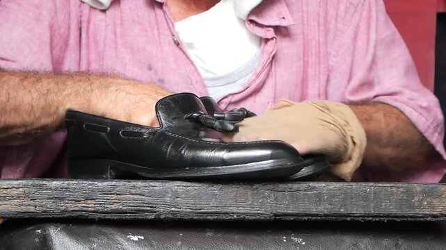 Man polishes black leather loafer shoes by hand with a cloth
