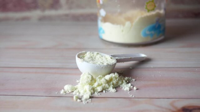 Baby powdered milk and spoon for formula preparation on wooden table background with baby bottle filled with milk powder